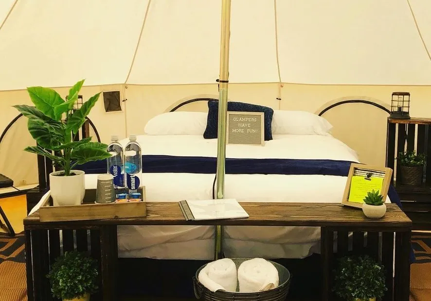E00DBD12-3938-4357-AE1B-9090739C7121_1_105_c Interior of a tent with a bed, plants, water bottles, and decorative items.