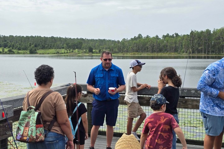 People fishing on a lakeside boardwalk with rods and gear.
