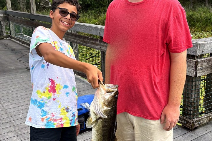 Two people on a boardwalk holding a large fish together.